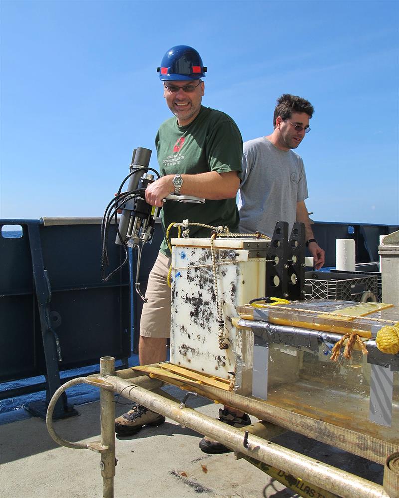 WHOI microbiologist Stefan Sievert carries an IGT back to the ship's lab. At right is WHOI geochemist Jeff Seewald, who developed the IGT samplers. The team uses an elevator to shuttle equipment and samples from the seafloor to the surface and back. - photo © Jennifer Barone, © Woods Hole Oceanographic Institution