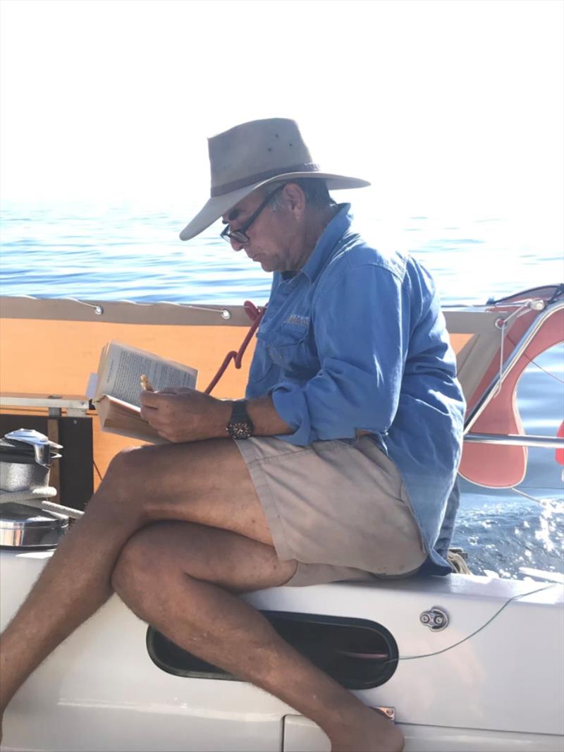 The Captain hard at work on passage, eating anzac biscuits and reading his novel! - photo © Red Roo